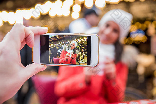 圣诞节市场上，一位美丽的年轻女子对着电话微笑着要拍照。