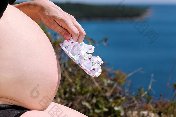 孕妇在怀孕的肚子上抱着未出生的小鞋子。幸福未来的妈妈和父母正在等待宝宝，爱和幸福。<strong>待产</strong>
