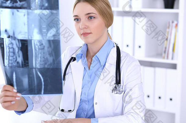 女医生正在医院窗户附近检查x光照片。工作中的外科医生或骨科医生。医学和保健概念。蓝色衬衫