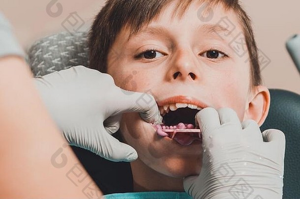 坐在牙医椅上的男孩，嘴里叼着印模盘