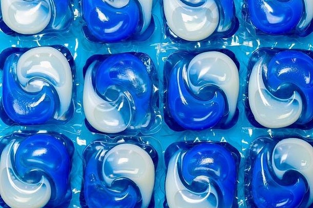 蓝色和白色洗衣机液体洗涤剂洗衣胶囊/豆荚在蓝色背景下的特写细节