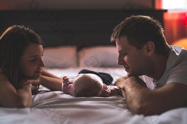 母亲、父亲和婴儿躺在白色的床上。