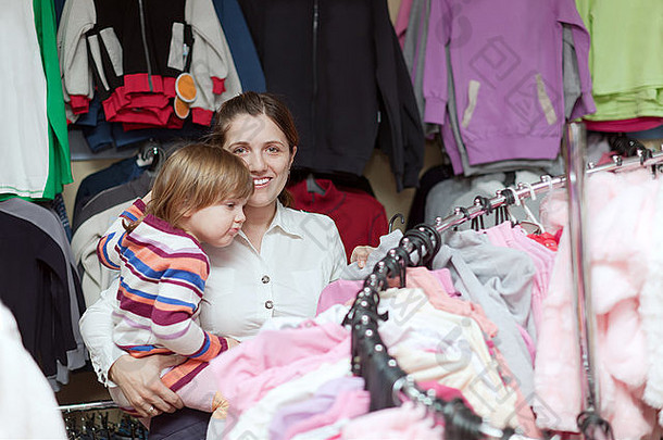 快乐的母亲和2岁的女儿在服装店挑选衣服