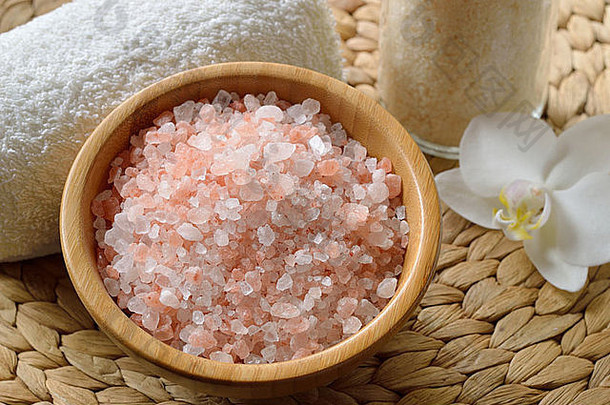 来自喜马拉雅山的粉红色盐。木制碗中粉色温泉盐的特写，配兰花和毛巾。