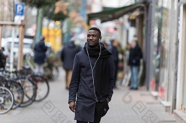 带着耳机和冬衣的年轻黑人走在街上，看着别处。