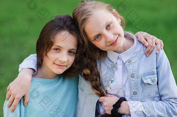 两个漂亮的白人朋友在绿草背景上拥抱着头发相连的小女孩
