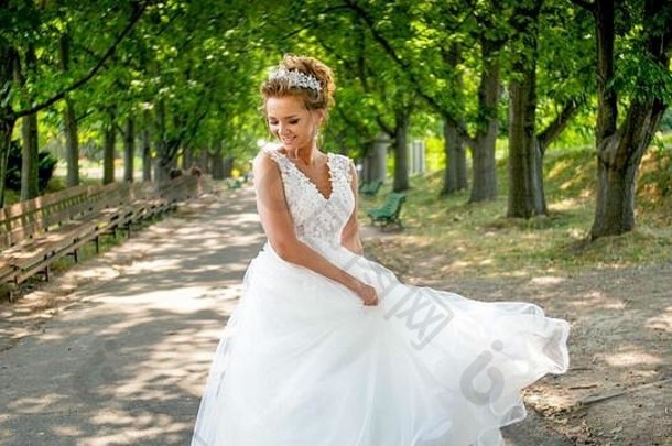 肖像快乐微笑年轻的新娘走公园挥舞着长白色新娘衣服
