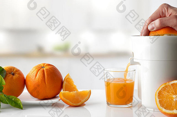 在白色餐桌上，用电动榨汁机在玻璃杯中用手挤压橙子。把橙子放在盘子里，然后切。水平的
