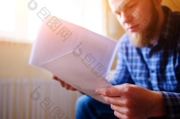 年轻英俊的男子坐在沙发上看着一份工作报告。