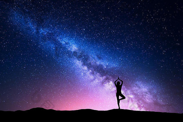 银河，一个站在山上练习瑜伽的女人的剪影。美丽的风景与沉思的女孩相映成趣
