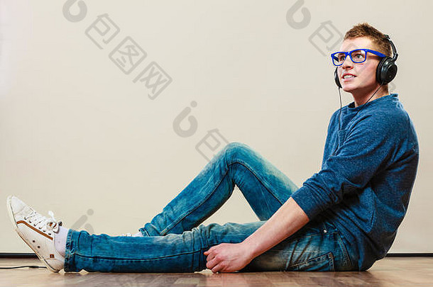休闲生活方式概念年轻的赶时髦的人男人。时尚衣服耳机坐着地板上听音乐