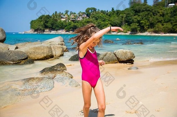 可爱快乐的小女孩穿着粉色<strong>游泳</strong>衣在海滩上跑步、跳舞。美丽的<strong>夏日</strong>阳光明媚，碧海，岩石，白沙，如画如画