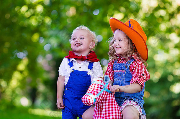 小男孩和小女孩装扮成牛仔和牛仔女孩，在公园里玩玩具摇马。孩子们在户外玩耍