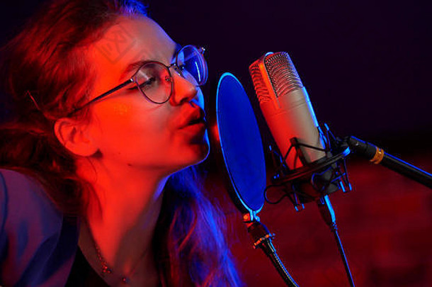 一个戴着圆眼镜的年轻女子在黑暗的演播室里的霓虹灯下唱歌