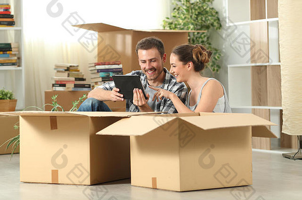 幸福的夫妇搬回家坐在地板上查看平板电脑内容