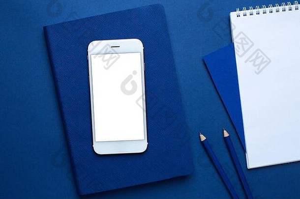 移动电话白色蓝色的办公室笔记本铅笔经典蓝色的背景前视图时尚的潘通色卡颜色