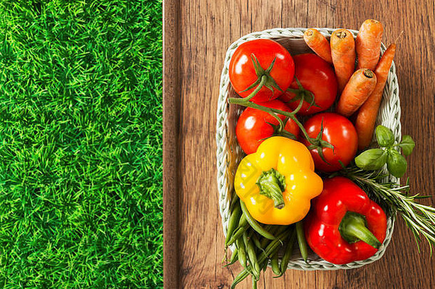 新鲜收获的蔬菜和草药放在白色的篮子里，绿草放在木桌上