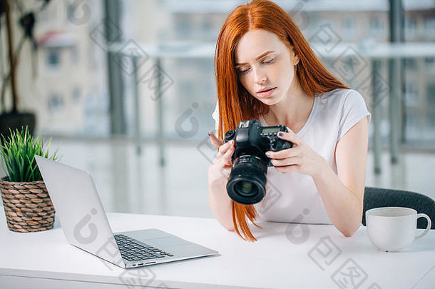 一个红头发的女人在笔记本电脑上工作时看着摄像机