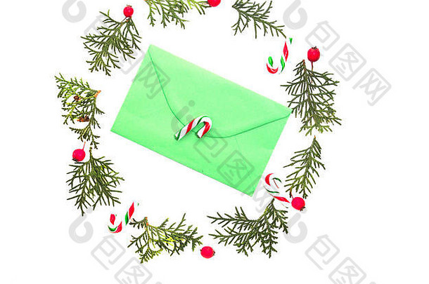 圣诞花环由Tuja嫩枝制成，红色野生玫瑰果实，绿色信封和糖果甘蔗在中间。白色背景。俯视图，平面布置。