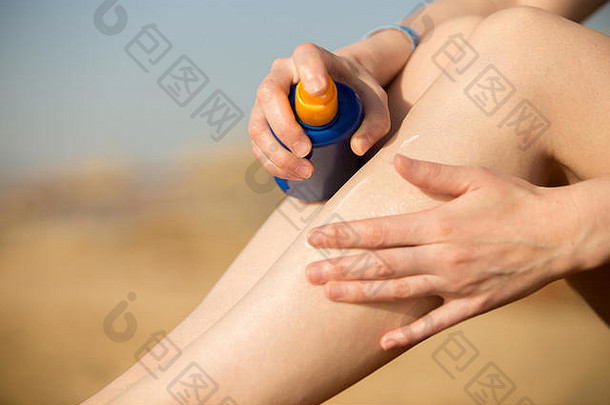 在阳光明媚的南部沙滩上晒黑前，一名年轻女子手持一瓶<strong>防晒乳</strong>液，在腿部涂抹<strong>防晒</strong>霜