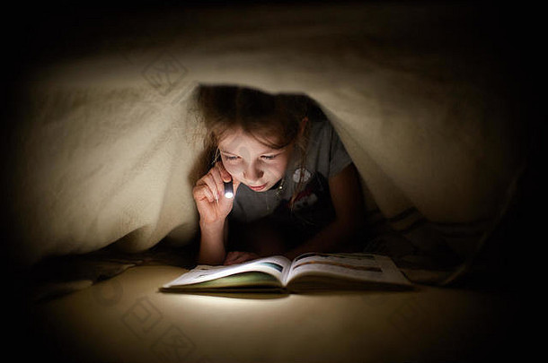 晚上，小女孩在黑暗的房间里用手电筒在毯子下看书