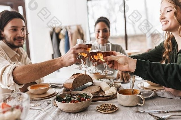特写镜头：一群<strong>国际友人</strong>坐在桌旁，手里拿着一杯酒，桌上摆满了食物。年轻的同事们快乐地度过时光