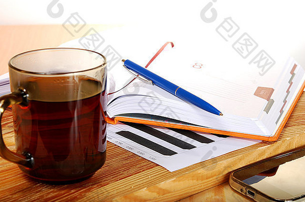 一杯茶放在一张木桌上，桌上放着一本笔记本和一支笔