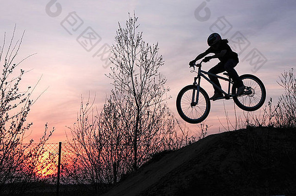 年轻的骑自行车的人在日落时骑着自行车跳跃