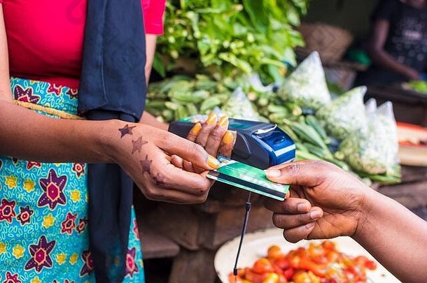 特写镜头：一名非洲妇女手持移动销售点设备在当地非洲市场上销售，从一名客户那里领取