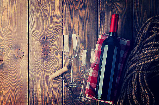 红葡萄酒瓶、玻璃杯和开瓶器，位于质朴的木制桌子背景上，并留有复印空间。复古色调