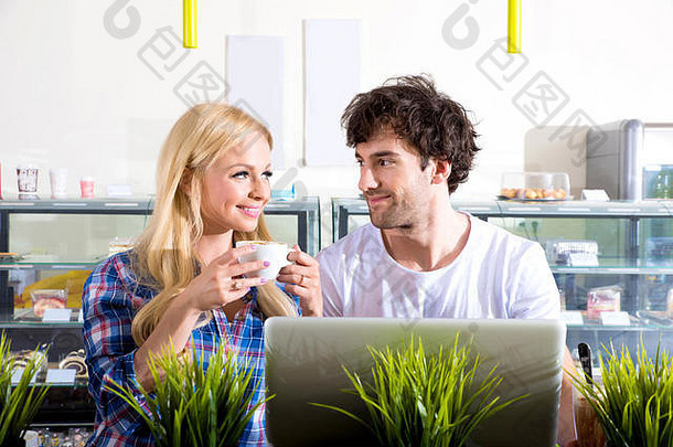 一对美丽的年轻夫妇坐在咖啡馆里用笔记本电脑