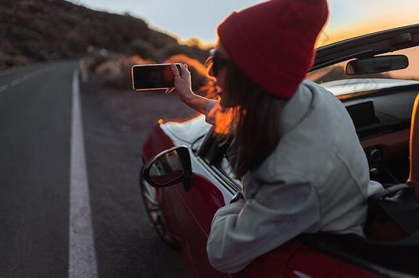 年轻的女人享受美丽的日落视图倾斜车窗口移动电话无忧无虑的生活方式旅行概念