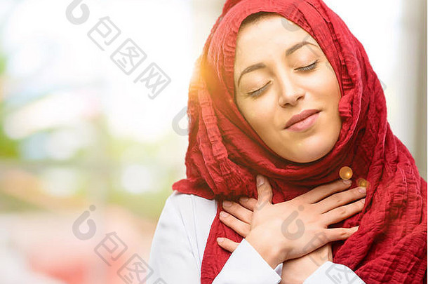年轻的阿拉伯妇女戴着盖头，双手插在心里，表达着爱和健康的理念