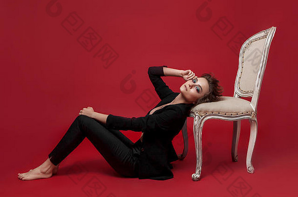 年轻的女孩黑色的西装红色的背景扶手椅