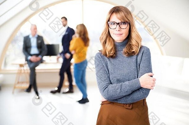 中年女商务主管站在办公室里，商务人士在后台咨询的肖像照。