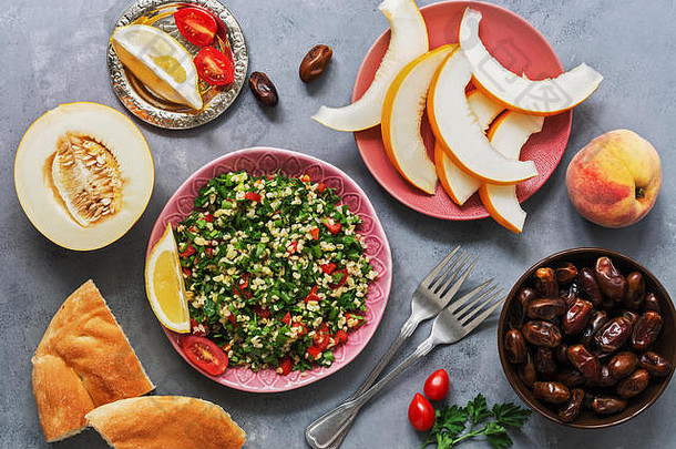 中东和阿拉伯食物tabbouleh沙拉、皮塔、甜瓜、桃子和<strong>枣</strong>，背景为<strong>灰</strong>色。俯视图，平面布置