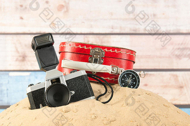 海滩沙滩上的复古红色手提箱、照相机和指南针
