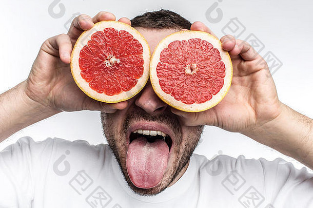 一张有趣的好照片，一个成年男子把两片半葡萄柚放在眼睛上。同时，他也在向镜头展示他的舌头。孤立的