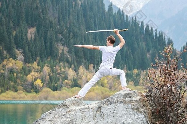 一个年轻人站在一块大石头上，手里拿着一把日本<strong>剑</strong>。
