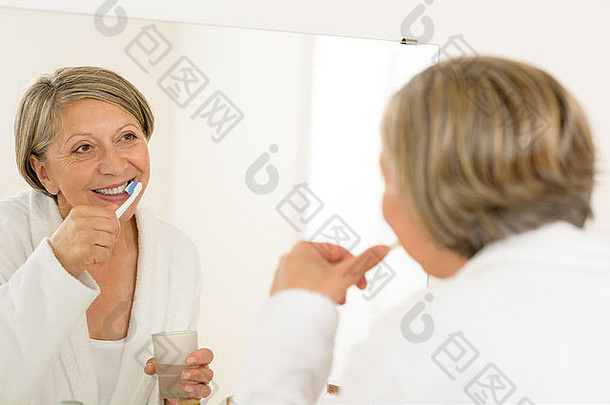 用牙膏刷牙的成熟女人看着浴室的镜子