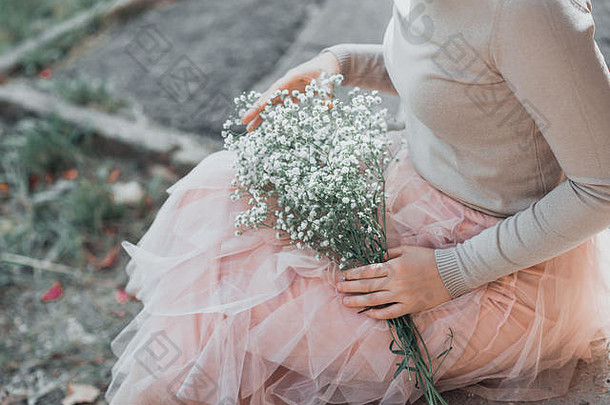 女人粉红色的花边裙子白色花花束手坐着楼梯