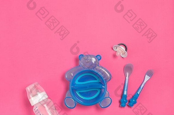 粉红色桌子上的蓝色熊形盘子、瓶子、刀和勺子。孩子们吃晚饭的时间。俯视图