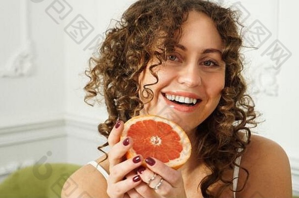 一位留着卷发的美丽中年妇女的肖像，在家里用葡萄柚装饰——灯光室。幸福、美丽和健康的概念
