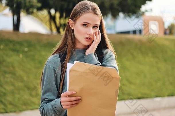 在公园里，心烦意乱的临时女学生打开信封，带着<strong>考试成绩</strong>悲伤地看着相机的照片