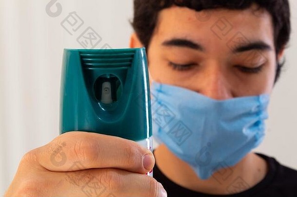 年轻的男人。穿蓝色的医疗面具持有瓶消毒液喷雾