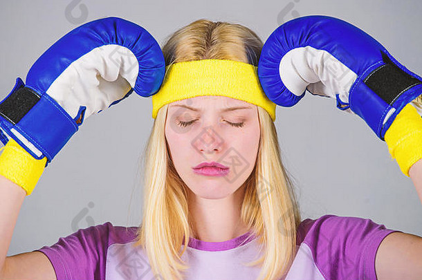 女孩痛苦的脸用拳击手套抱着头。头痛疗法。头痛的概念。保持镇静，消除头痛。治头痛。女孩打拳击手套累了。坚强的女人承受痛苦。