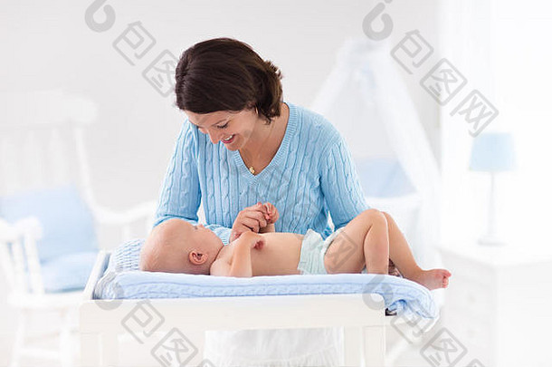 母亲和婴儿在有床和摇椅的白色托儿所洗澡后换尿布。小男孩穿着干净干燥的尿布在换桌子。妈妈照顾