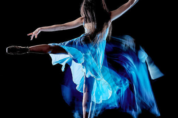 一名白人年轻女子芭蕾舞演员在黑色背景上独立跳舞，具有灯光画运动模糊速度效果