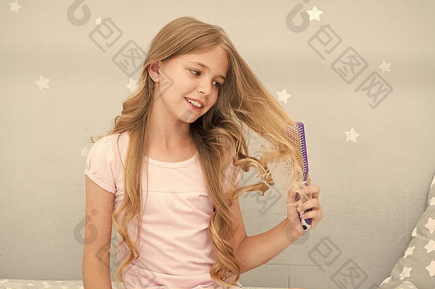 孩子卷曲的发型持有毛刷梳子应用石油梳理头发健康的头发护发素面具有机石油梳子头发美沙龙提示女孩长卷曲的头发灰色室内背景