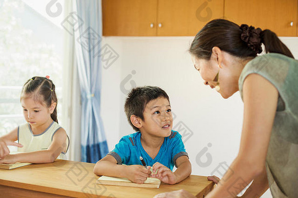一位老师正在和坐在书桌旁的两个孩子谈话。